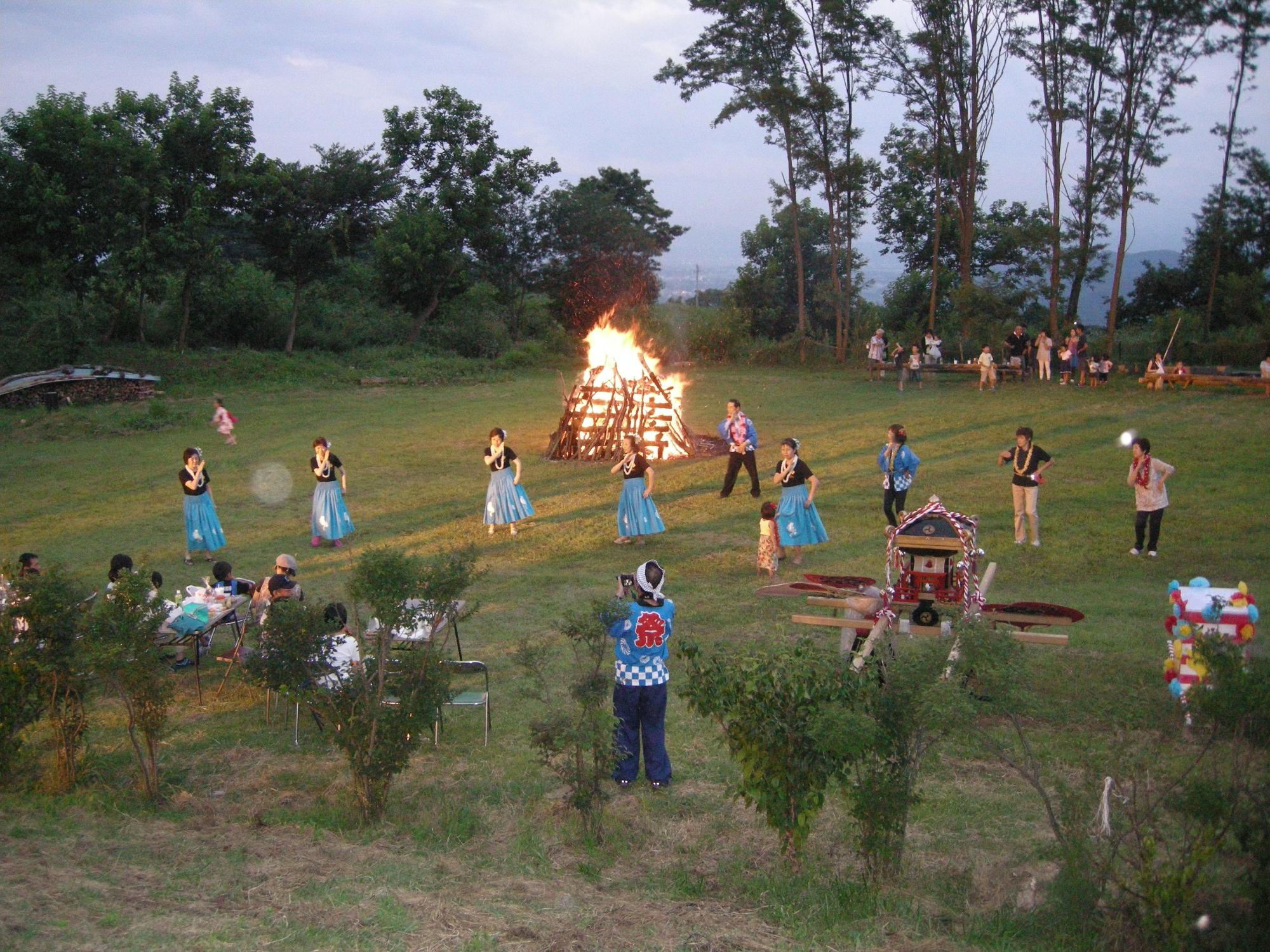 キャンプファイヤーの前でフラダンスを踊っているお祭りの写真