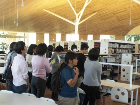 本棚やテーブルなどの備品を白で統一されたオープンしたばかりの安曇野市の図書館を視察している人達の写真